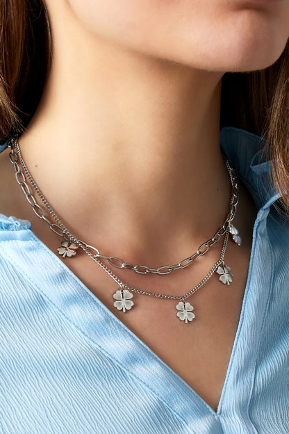 Silver toned layered necklace with clover charms worn by woman in blue top