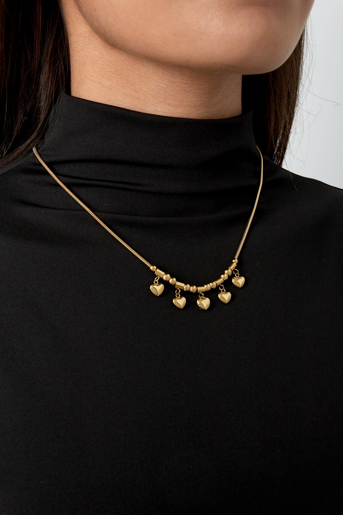 Model wearing gold heart charm necklace paired with a black high-neck top showing the necklace's size and fit