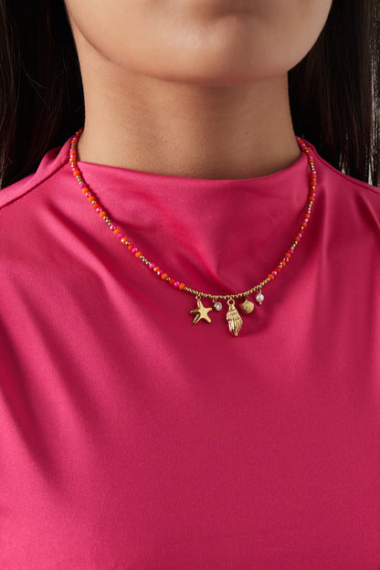 Lifestyle image of necklace worn on a woman with a bright pink top highlighting the vibrant beads and gold charms