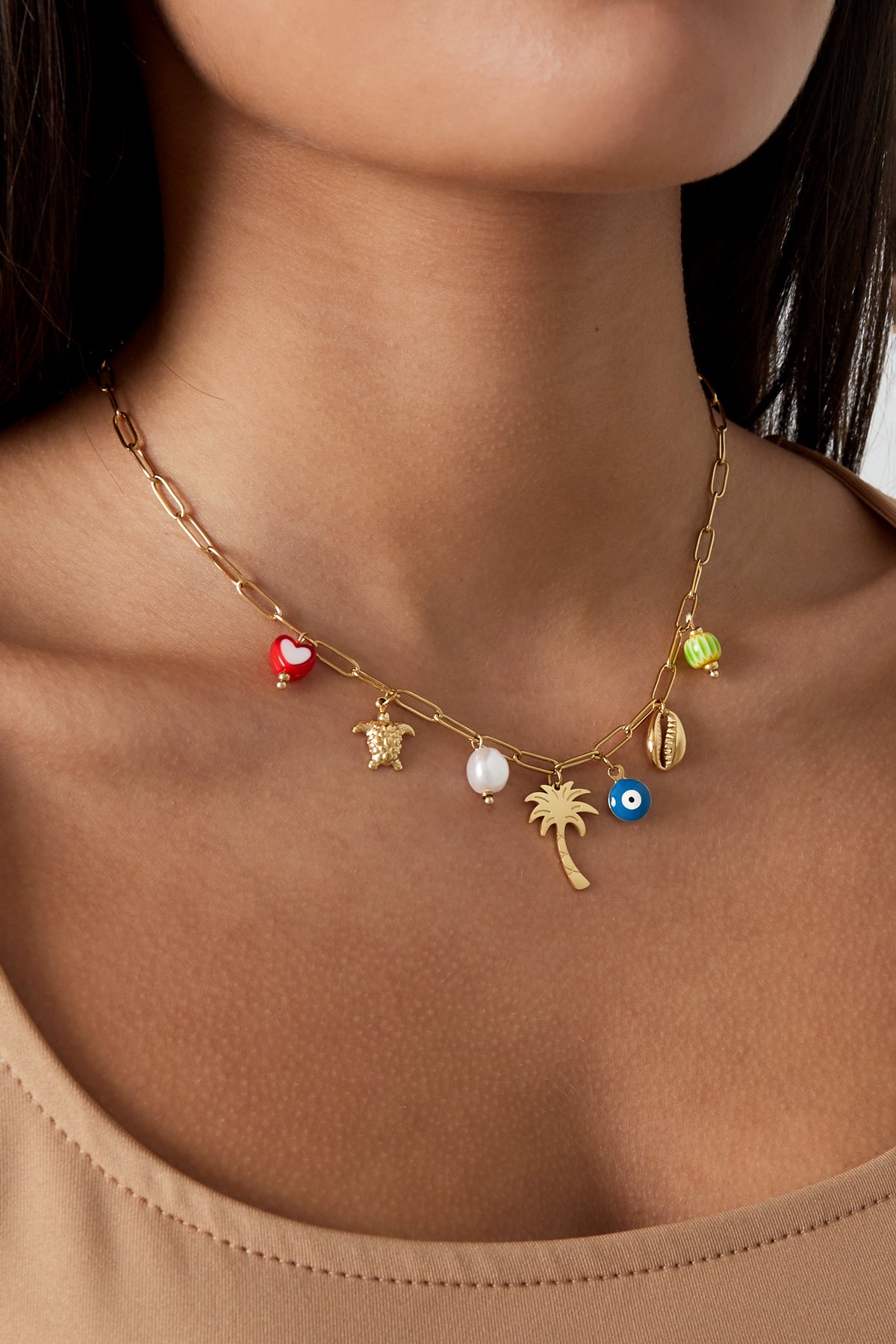Close-up of a woman wearing a gold-tone link necklace with playful charms resting along her collarbone with a beige top