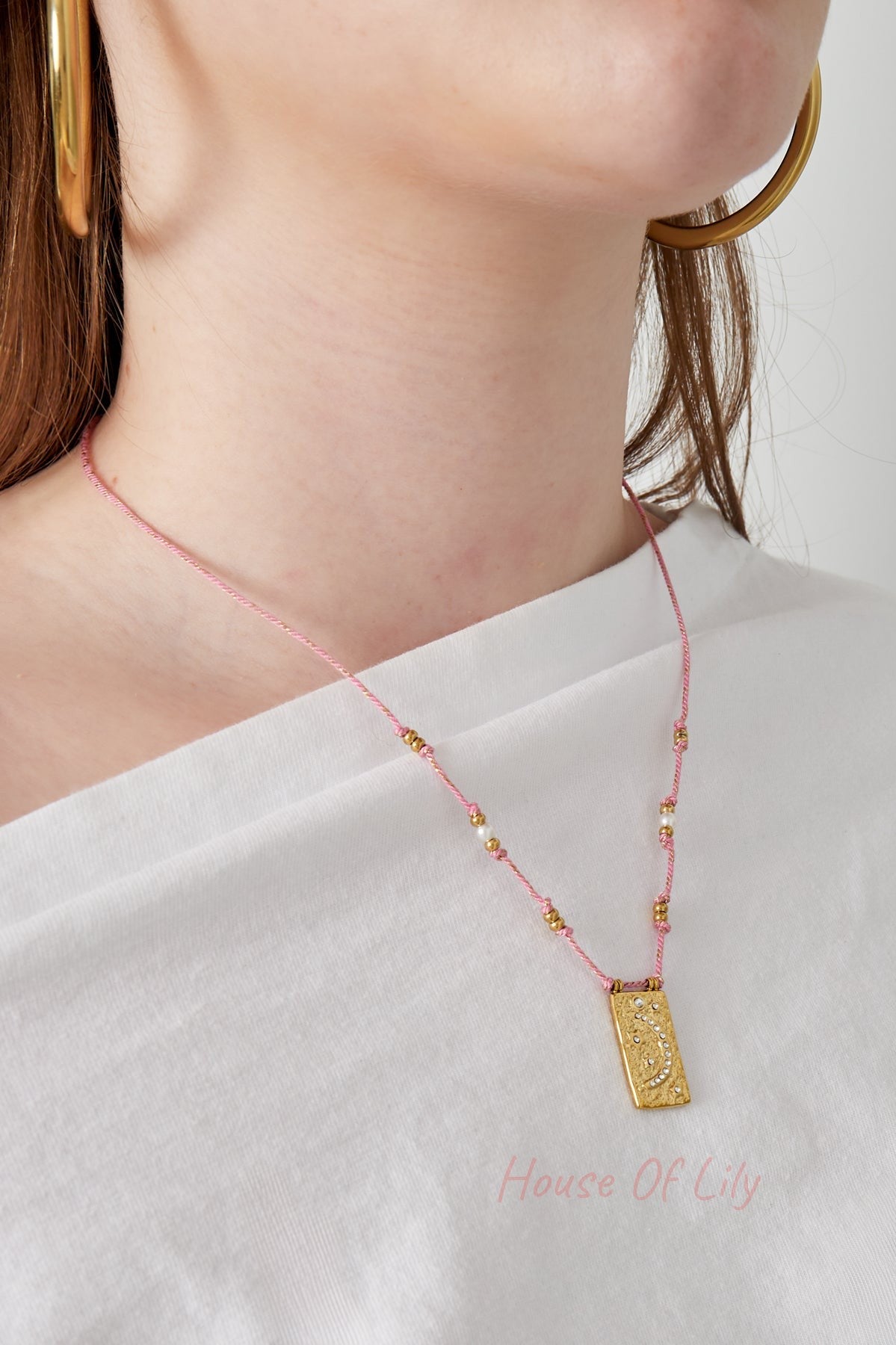 Model wearing the pink braided moon pendant necklace with white top and gold hoop earrings