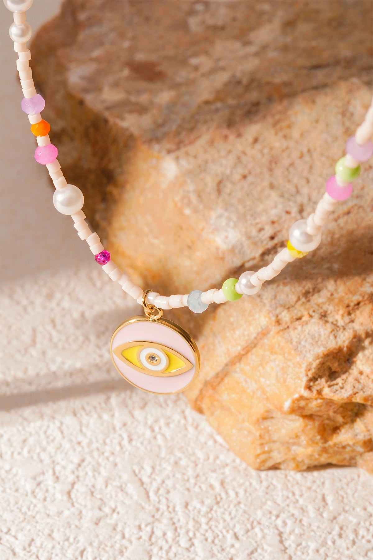 Golden eye charm detail on pastel beaded necklace against textured stone