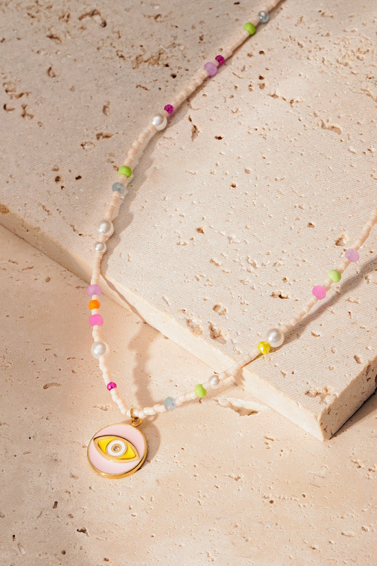 Pastel and pearl bead necklace with golden eye pendant on natural stone surface