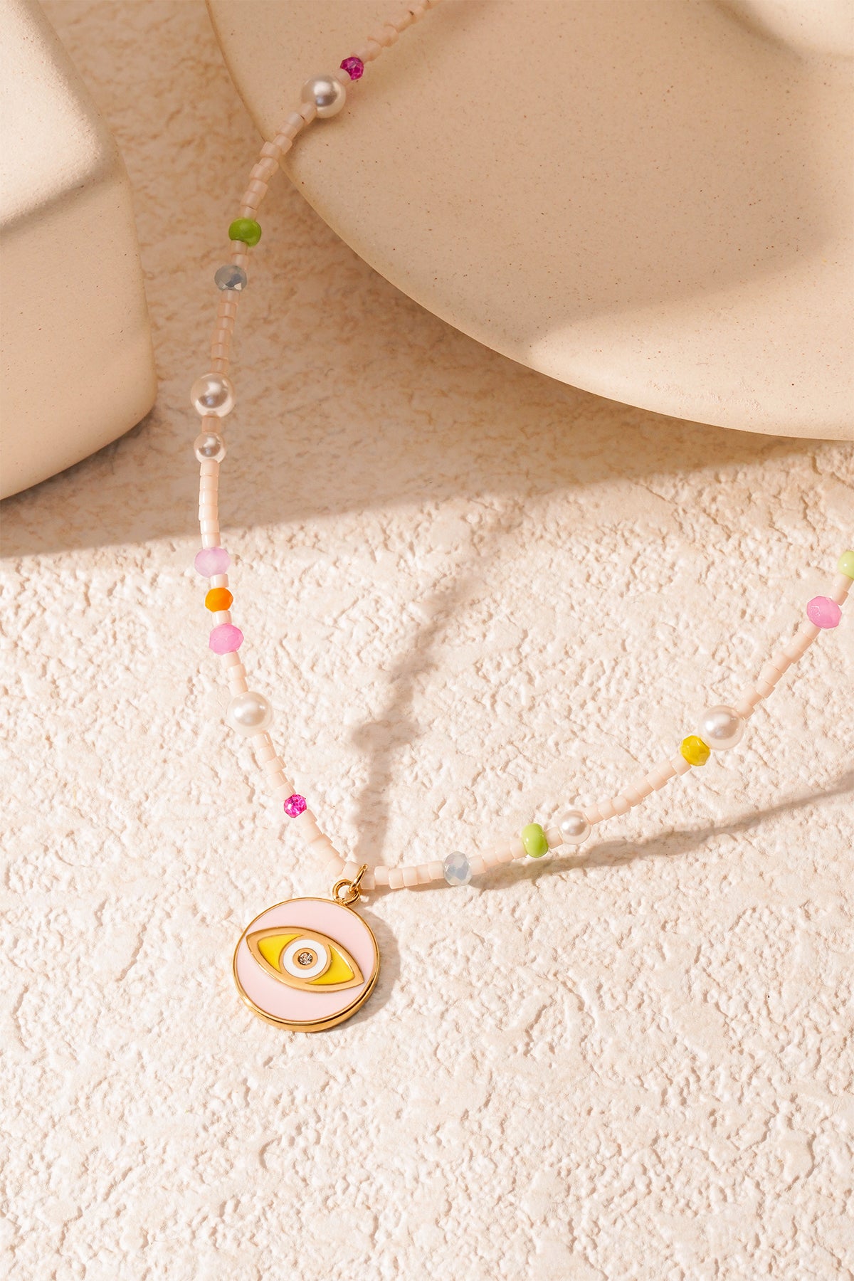 Artistic shot of pastel beaded necklace with eye charm casting shadow on textured background