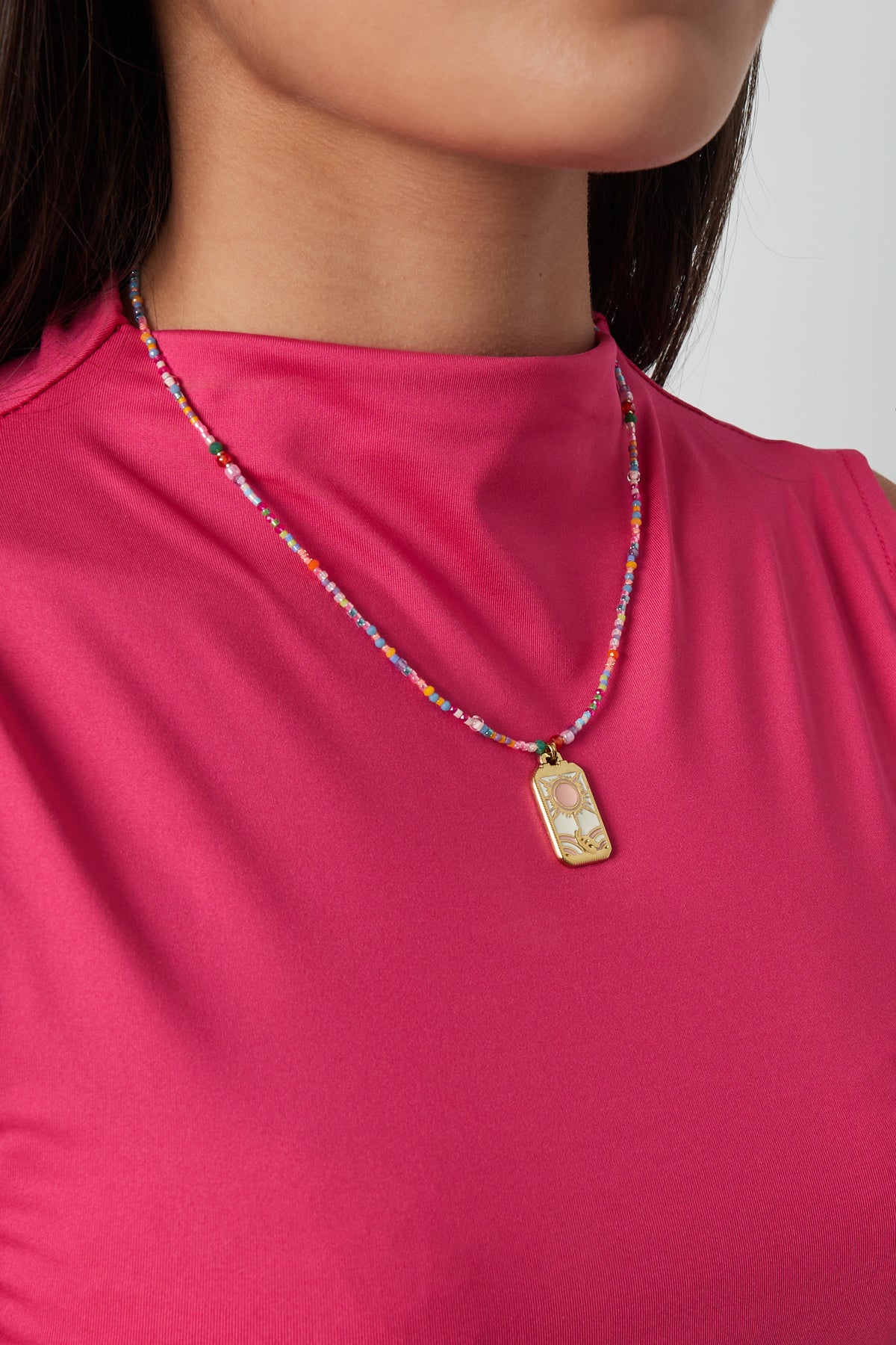 Woman wearing a vibrant beaded necklace with a sun charm pendant, styled with a bright pink top