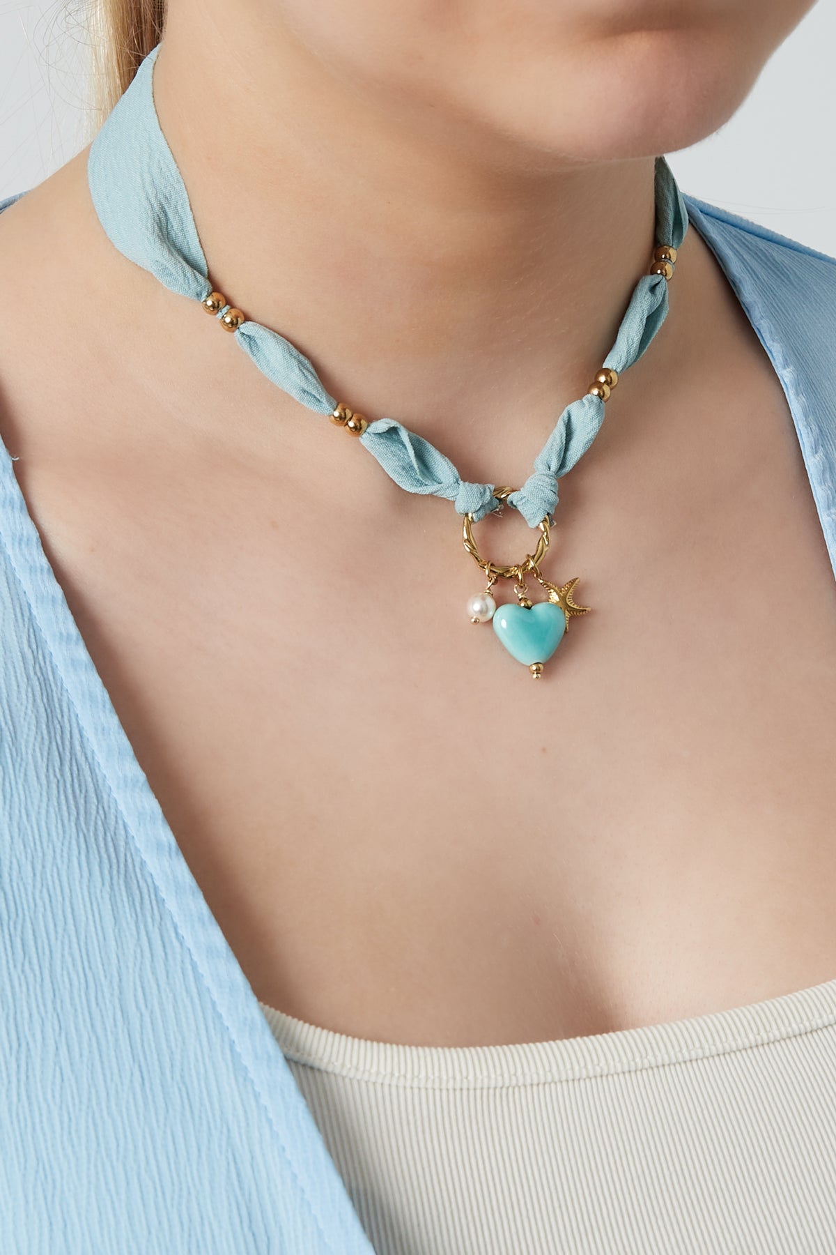 Model wearing light blue braided heart charm necklace paired with a matching light blue top.