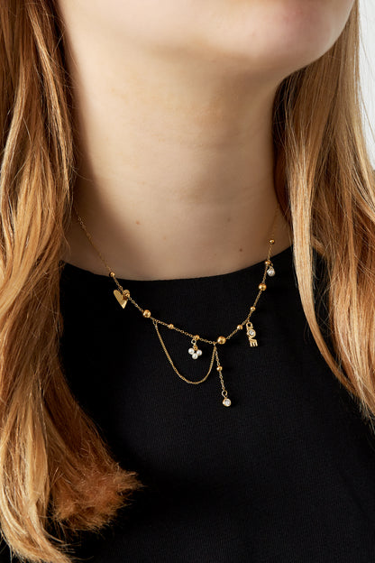 Close-up of model wearing gold pendant necklace with playful charm details against black top