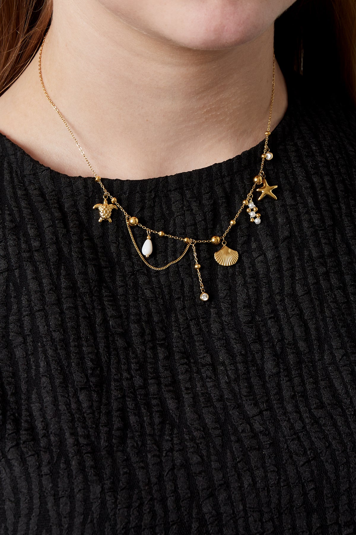 Model wearing gold ocean charm necklace with multiple charms over black textured top