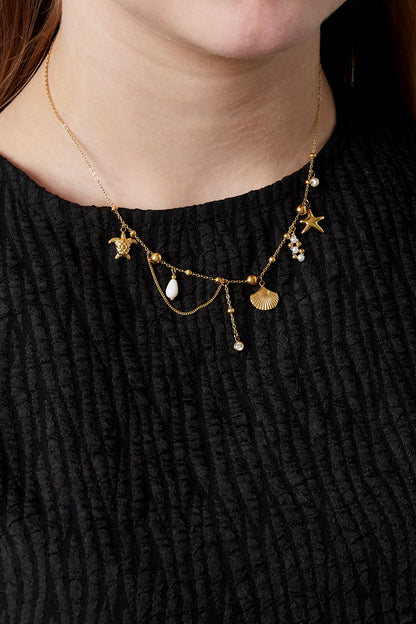 Model wearing gold ocean charm necklace with multiple charms over black textured top