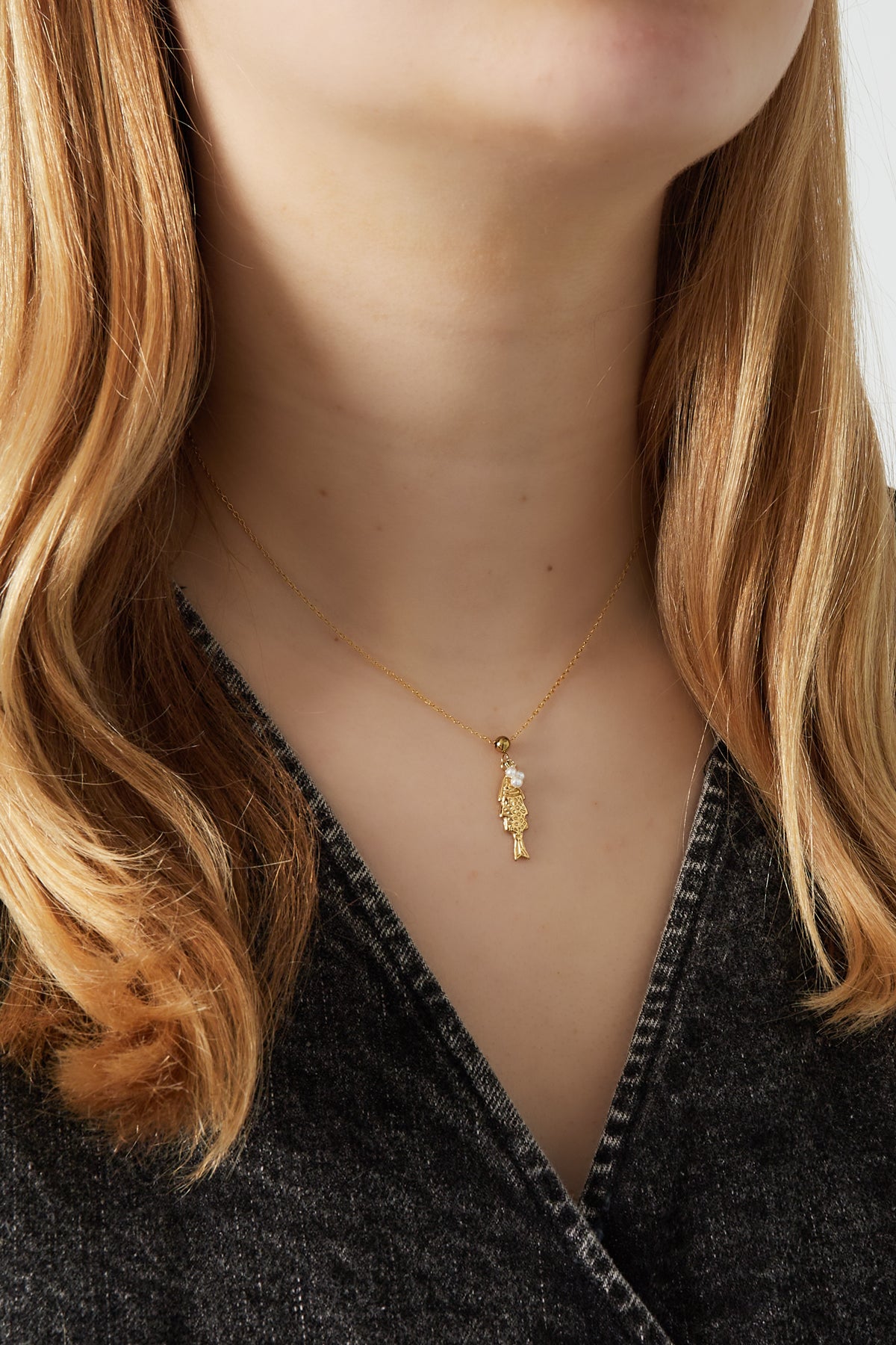 Close-up of a gold fish pendant necklace worn around the neck with pearl detail