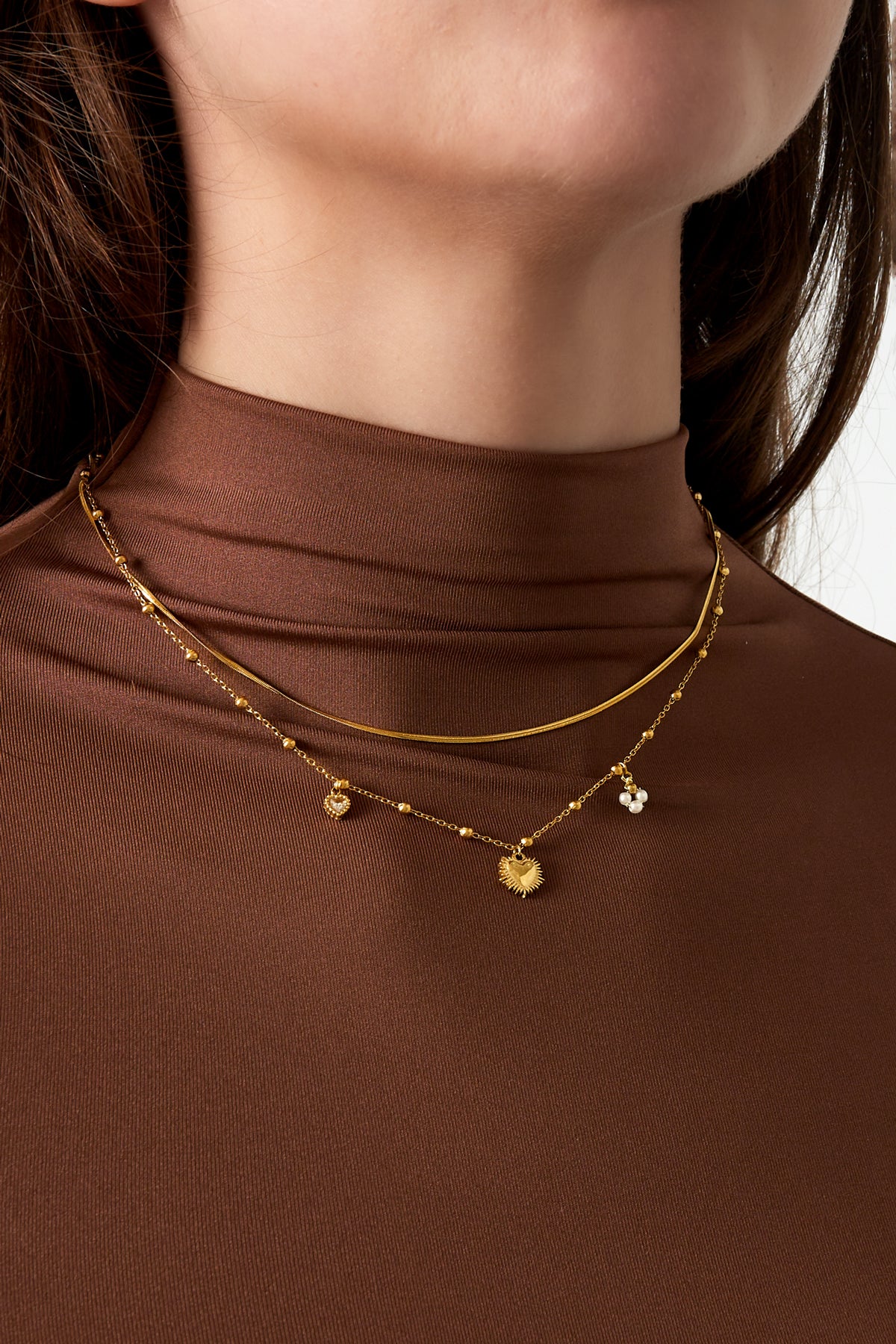 Close-up of woman wearing gold-tone layered heart charm necklace with brown turtleneck