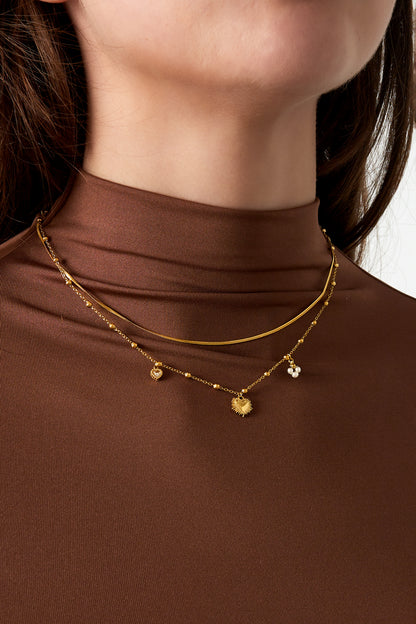Close-up of woman wearing gold-tone layered heart charm necklace with brown turtleneck
