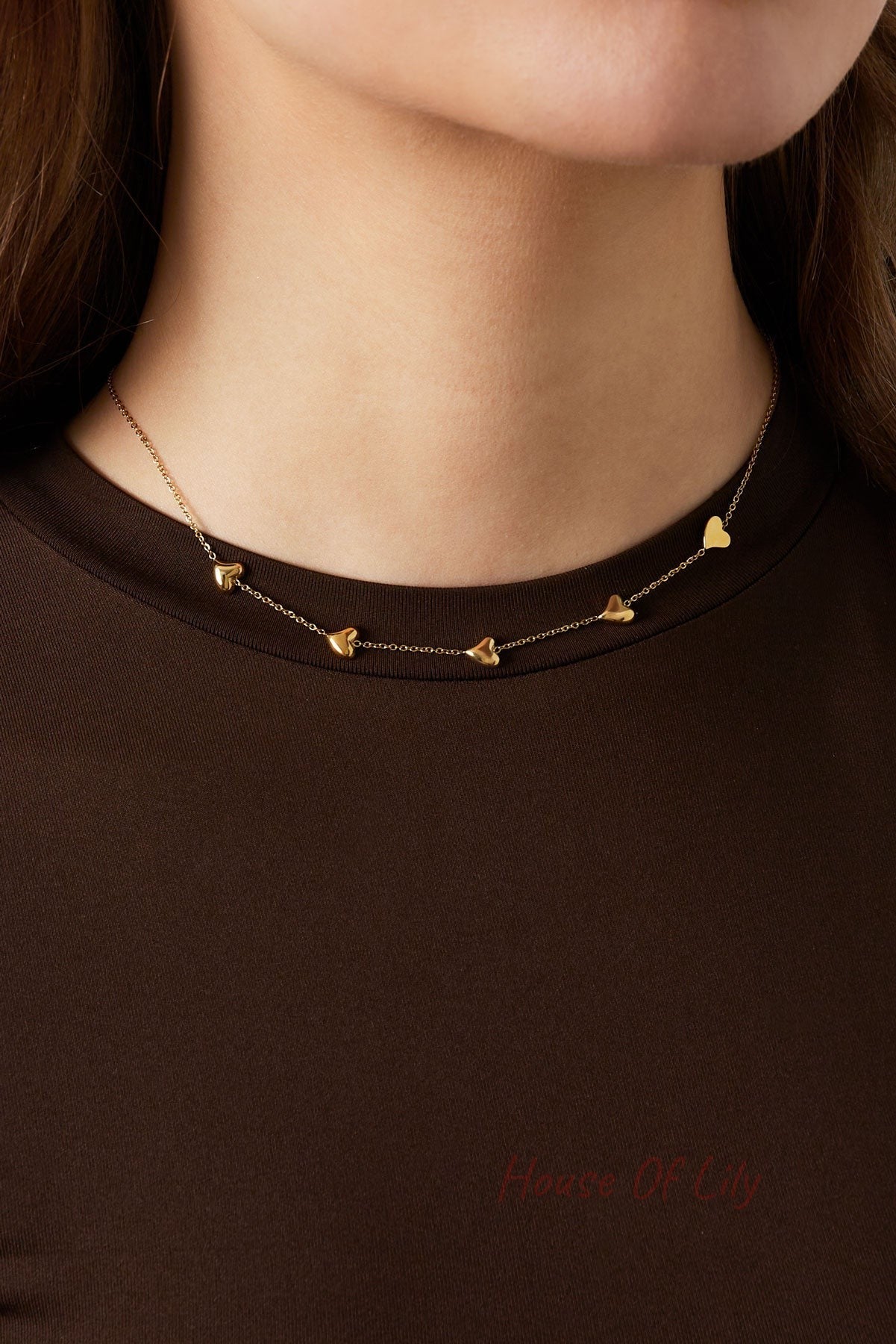 Close-up of a woman wearing the gold heart charm necklace styled with a dark brown top, showing delicate fit on clavicle