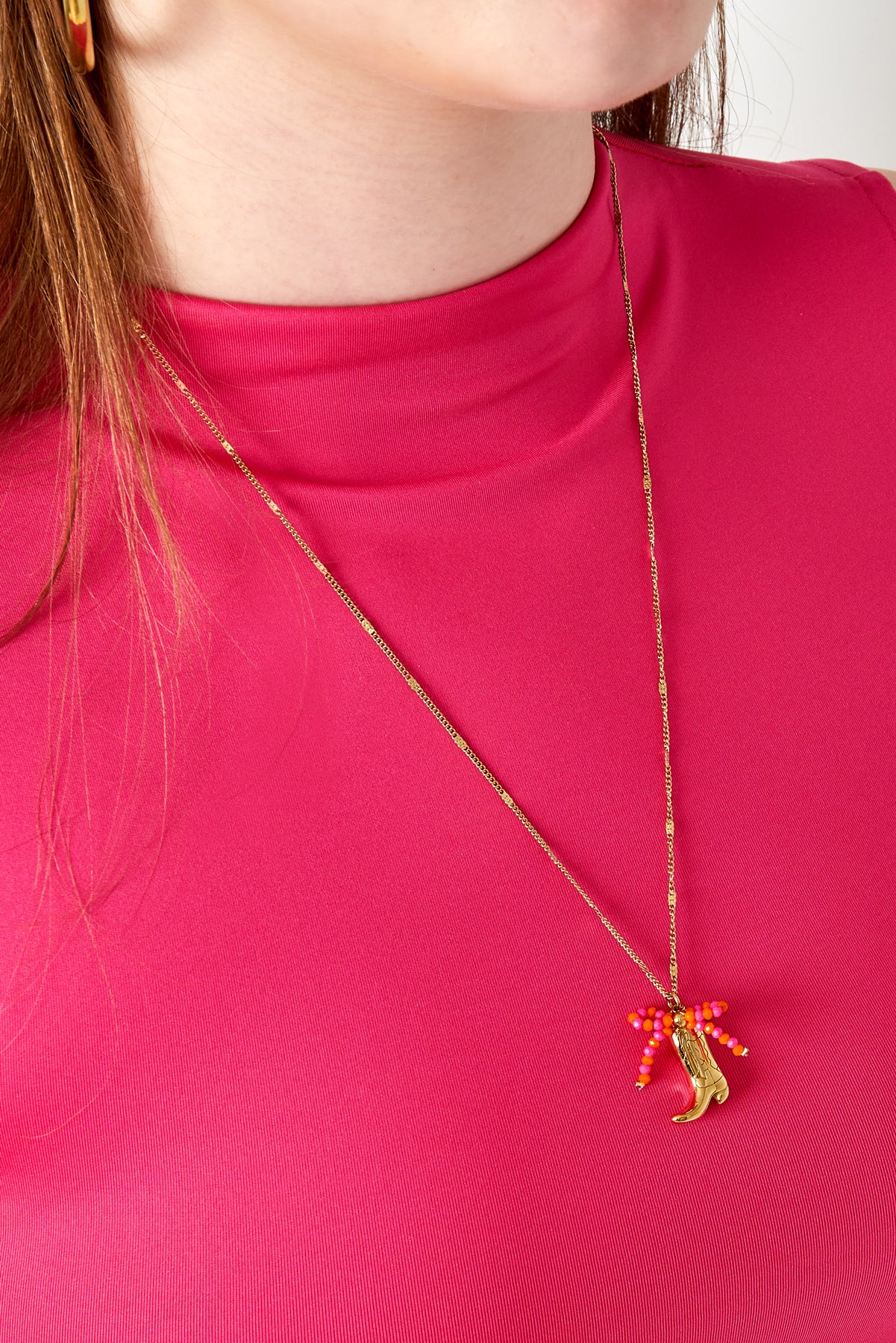 Woman wearing gold-tone cowboy boot pendant necklace featuring bright pink and orange beads with pink top
