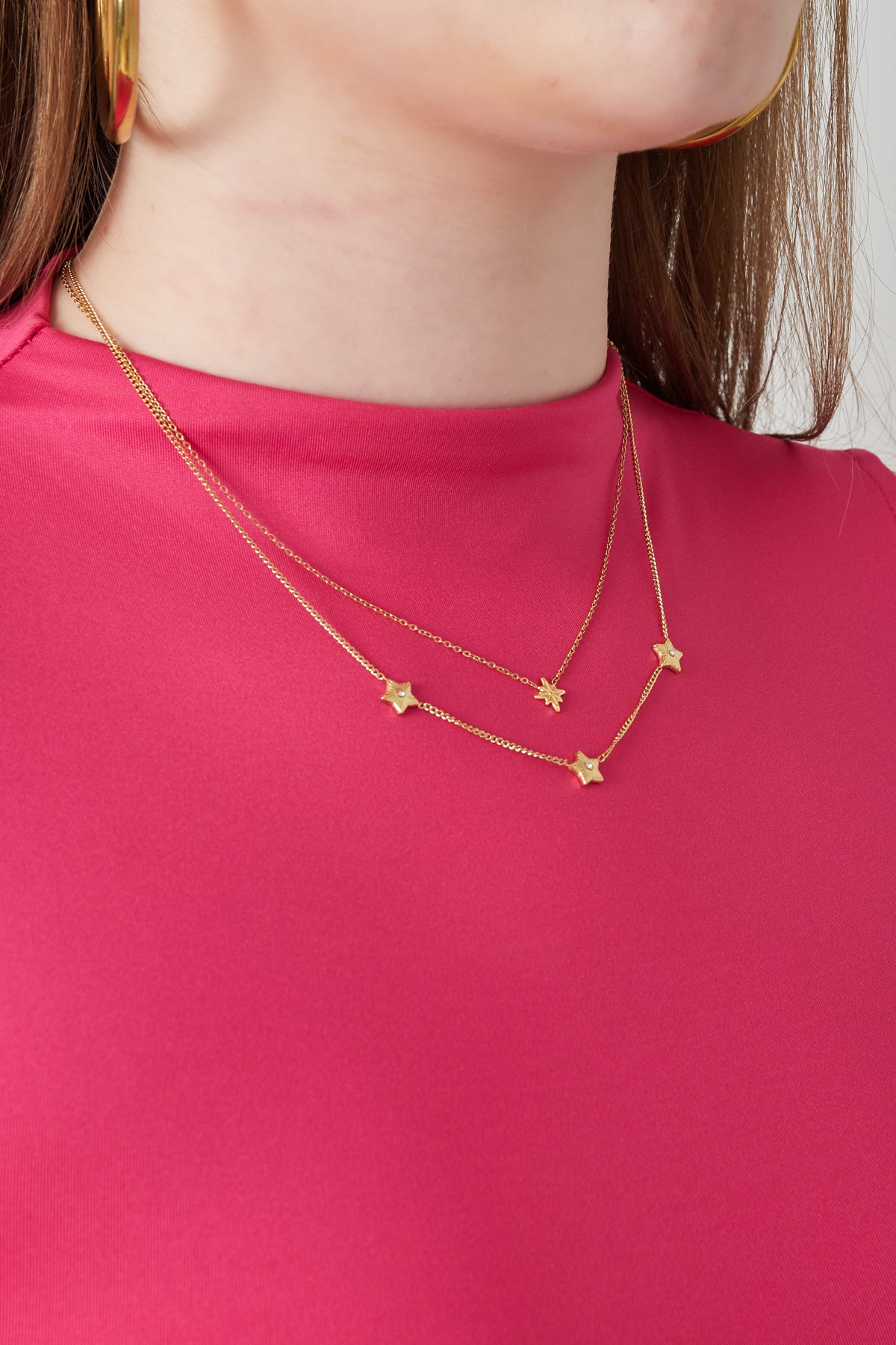 Model wearing gold layered star necklace paired with pink top and gold hoop earrings