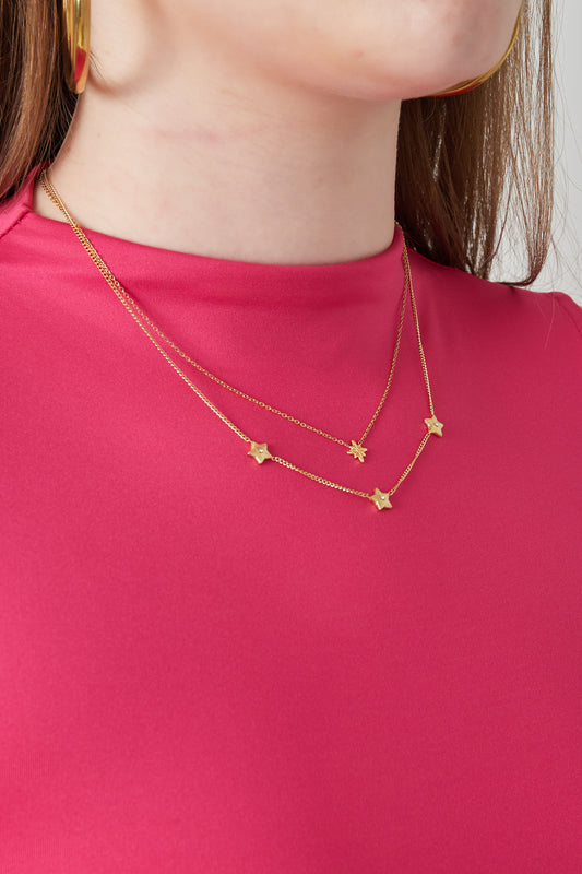 Model wearing gold layered star necklace paired with pink top and gold hoop earrings
