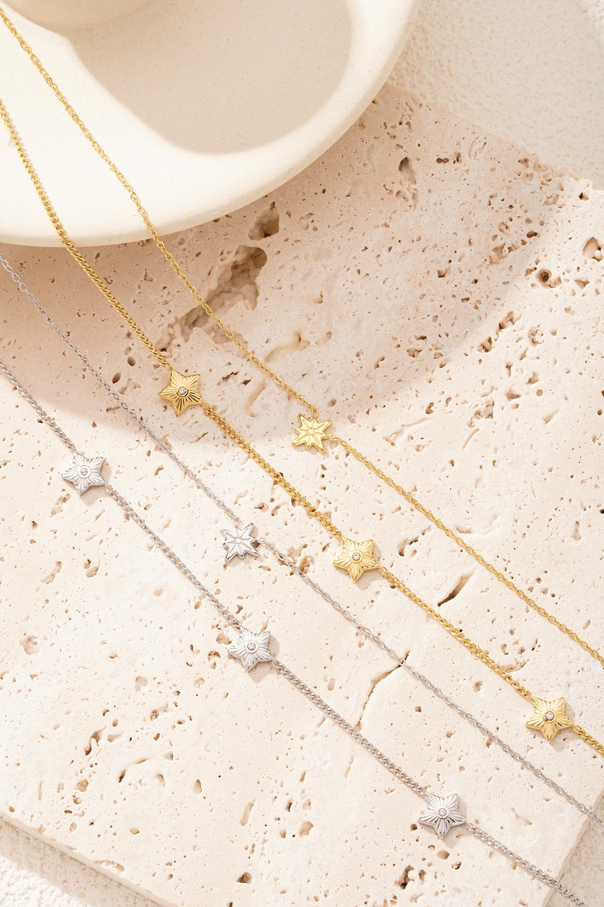 Close-up detail of gold and silver layered star necklaces on a beige textured background