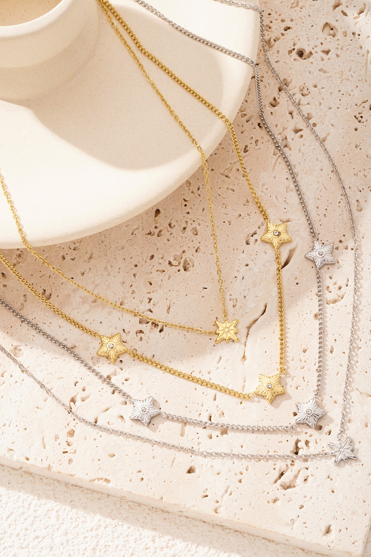 Gold and silver layered star necklaces arranged on beige textured surface