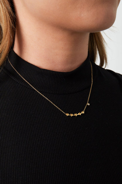 Close-up photo of a woman wearing the gold star cluster necklace over a black ribbed turtleneck top
