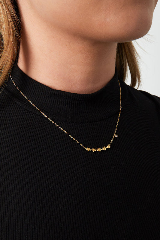 Close-up photo of a woman wearing the gold star cluster necklace over a black ribbed turtleneck top