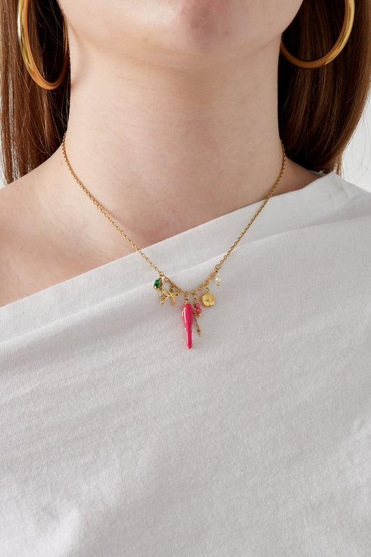 Woman wearing gold-tone charm necklace featuring pink pepper and other colorful charms paired with white top