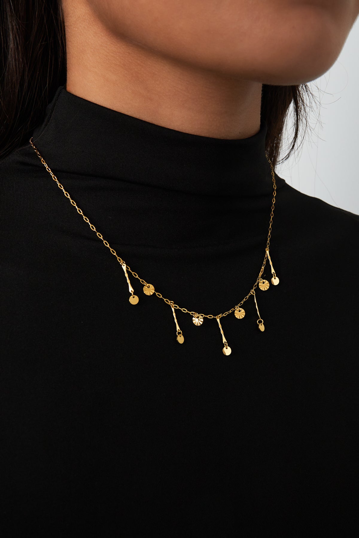 Close-up of gold charm necklace worn on model with black top showing chain and pendants