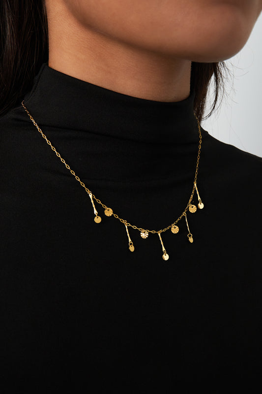 Close-up of gold charm necklace worn on model with black top showing chain and pendants
