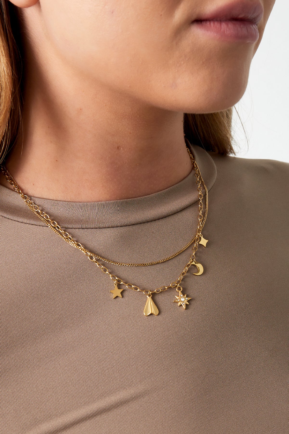 Close-up of a woman wearing the gold layered celestial charm necklace paired with a taupe top