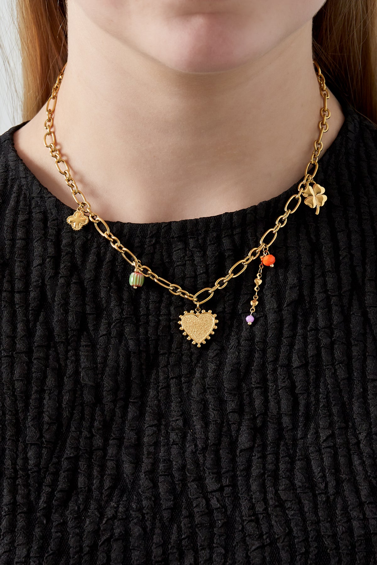 Model wearing golden charm link necklace styled with a black top showing chain length and charm details.