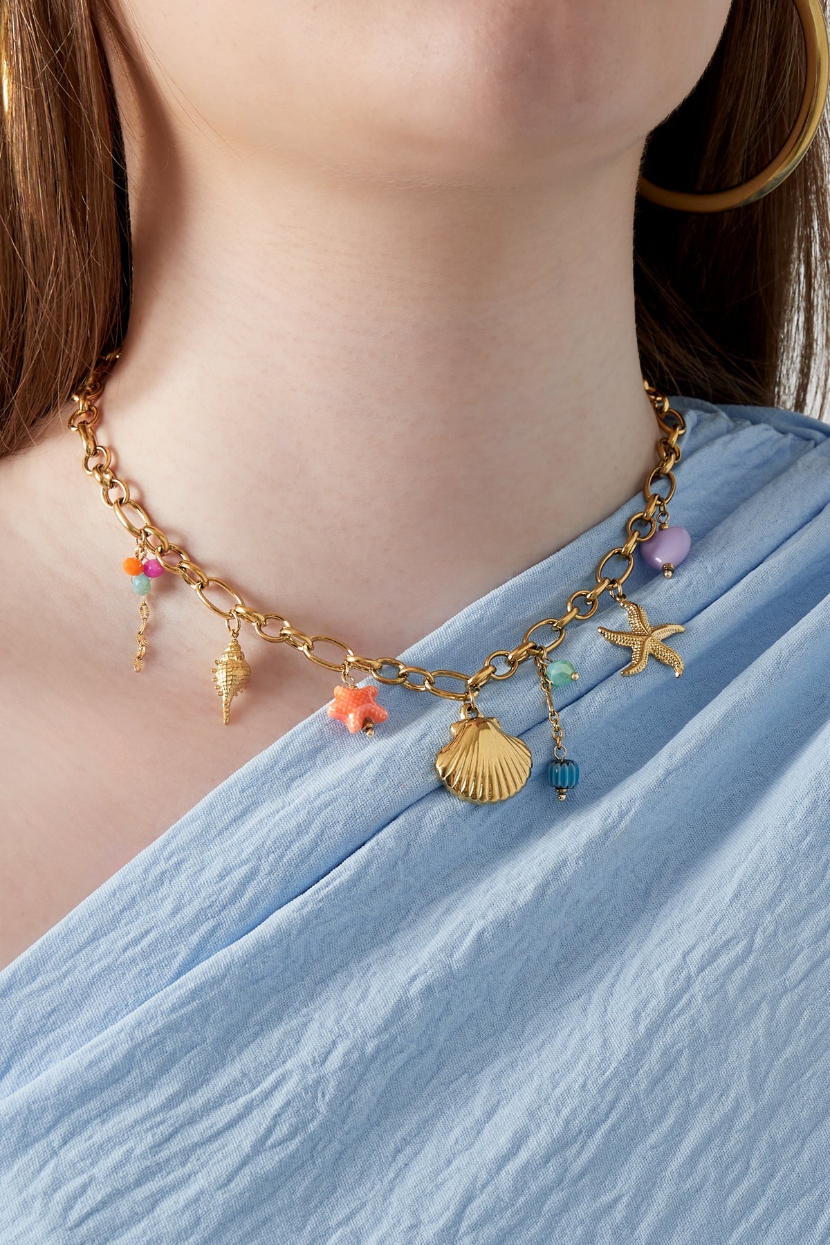 Model wearing gold sea charm necklace with light blue top and gold hoop earrings