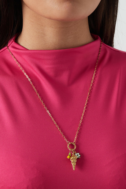 Model wearing gold shell charm necklace with enamel bead accents styled with bright pink top