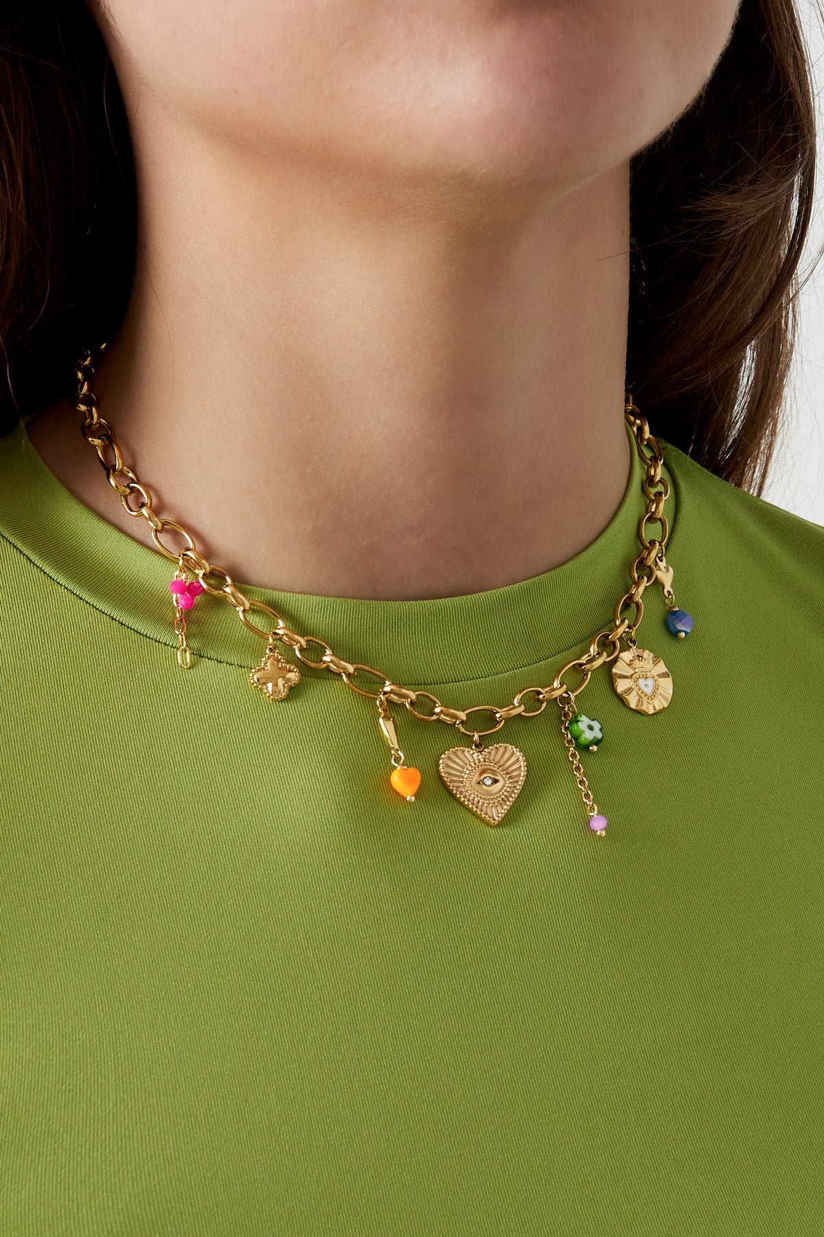 Close-up of a woman wearing playful gold-tone charm necklace with colourful heart and flower pendants against a green top