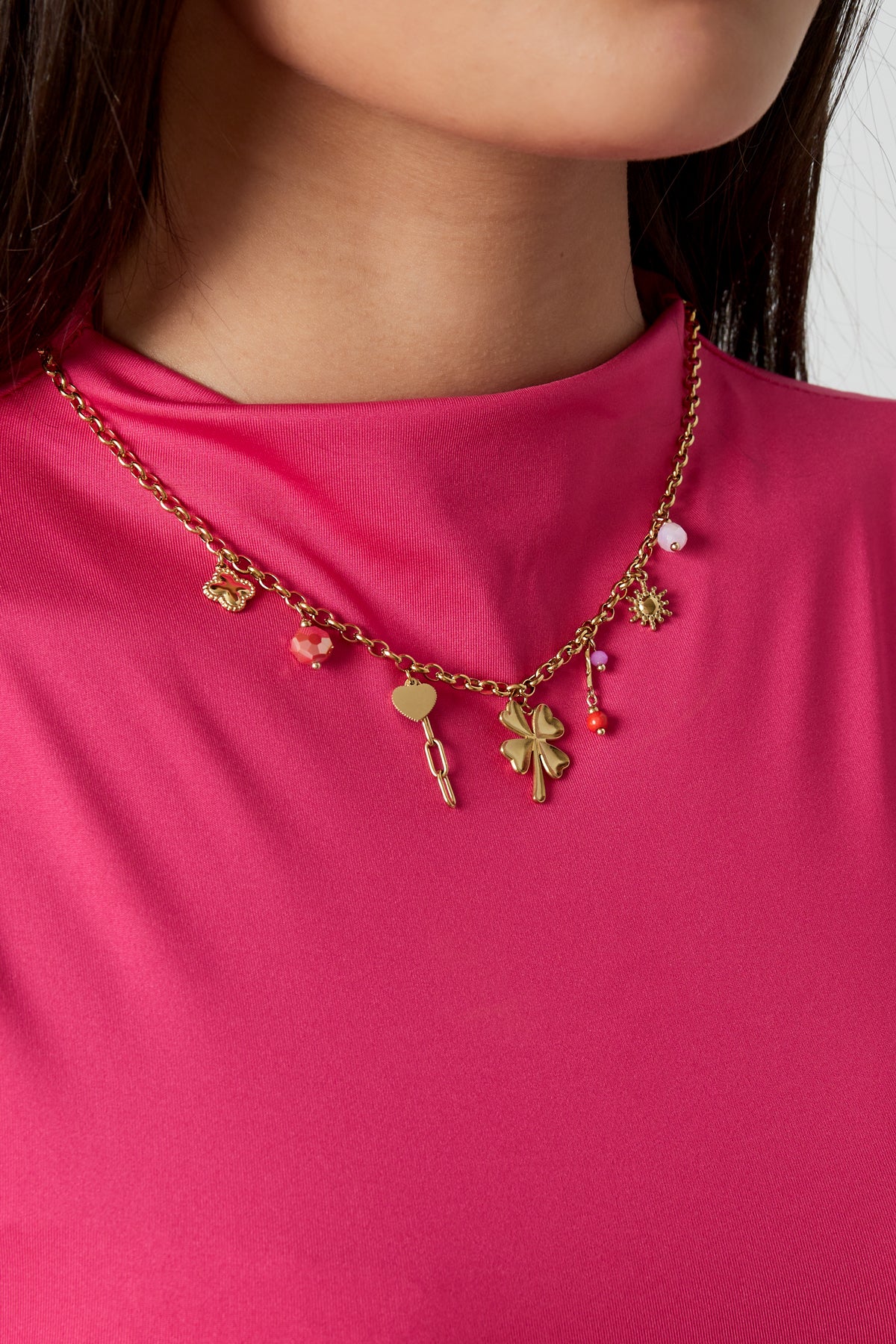 Model wearing gold-tone four leaf clover charm necklace paired with a bright pink top