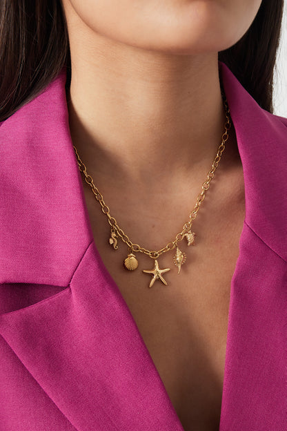 Model wearing the gold-tone ocean charm necklace paired with a magenta blazer