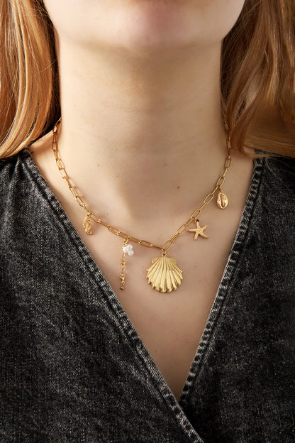 Woman wearing the gold seaside charm necklace showcasing the shell and starfish pendants resting on the clavicle.
