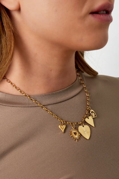 Model showcasing the gold link necklace with distinctive charms over a beige top