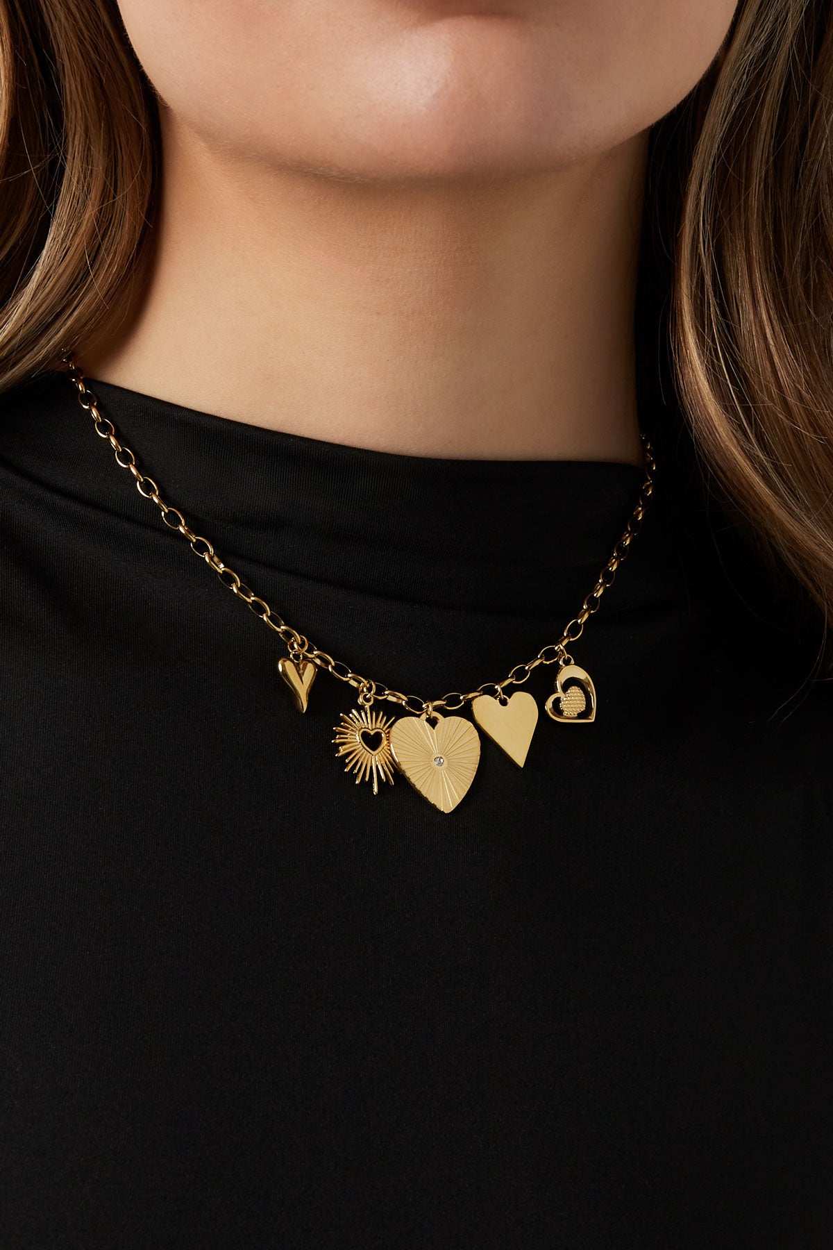Model wearing the gold link necklace with heart and sunburst pendants over a black top