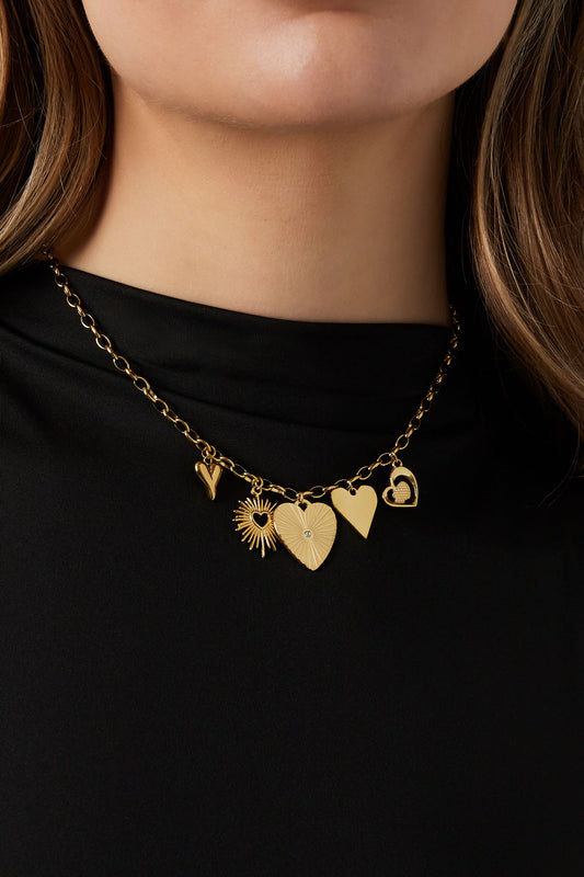 Model wearing the gold link necklace with heart and sunburst pendants over a black top