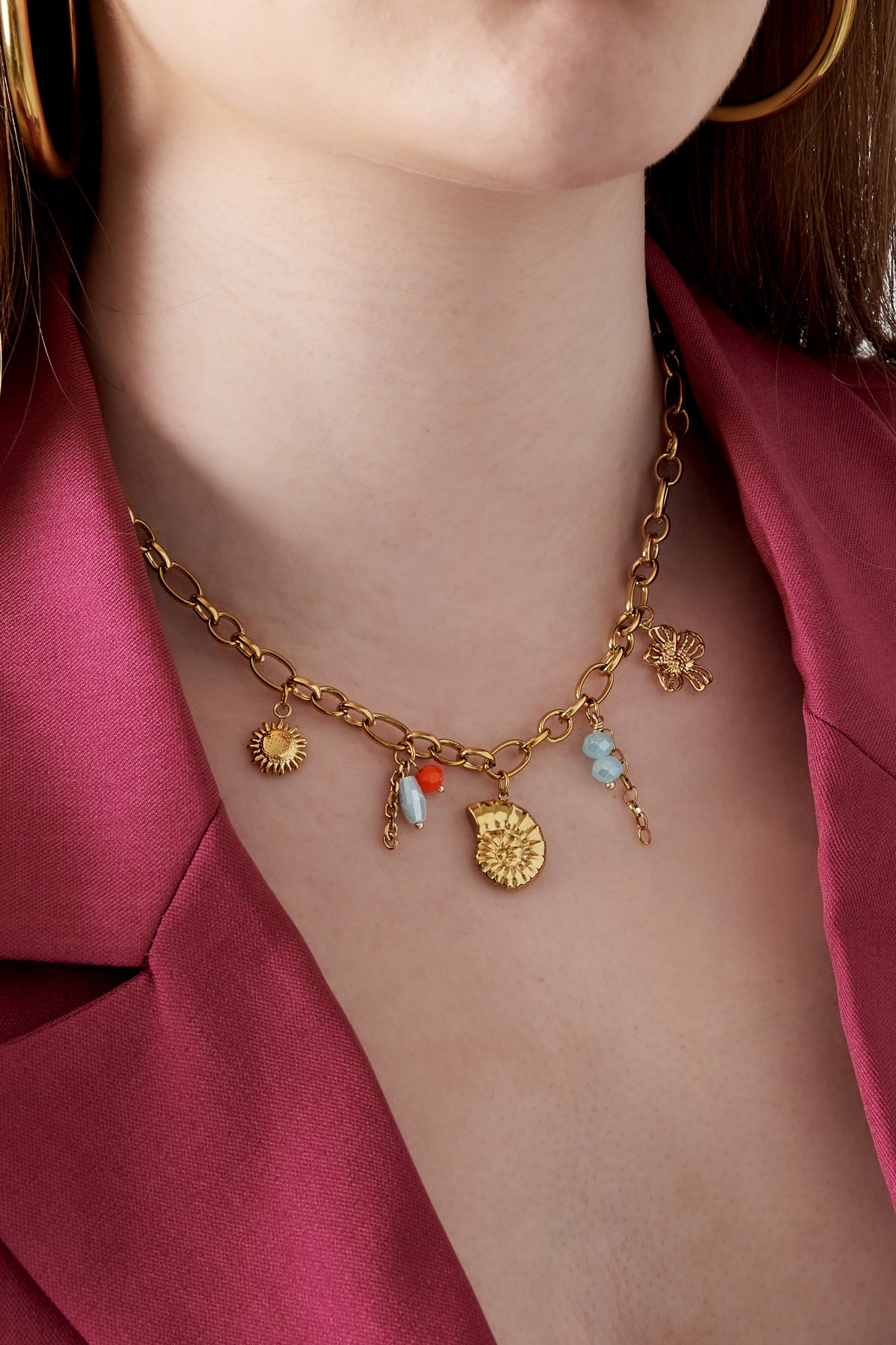 Model wearing gold charm necklace paired with bold pink blazer