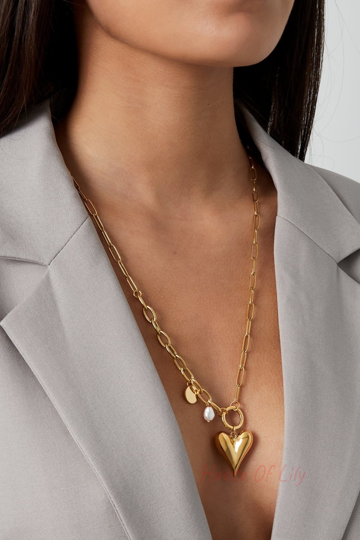 Close-up of female model wearing gold-tone chunky heart pendant necklace styled with grey blazer
