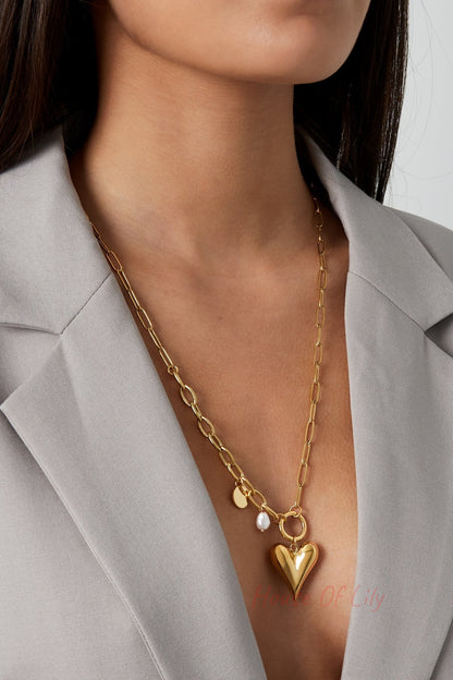 Close-up of female model wearing gold-tone chunky heart pendant necklace styled with grey blazer