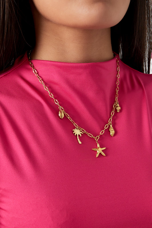 Model wearing gold seaside charm necklace paired with bright pink top showing stylish, youthful look