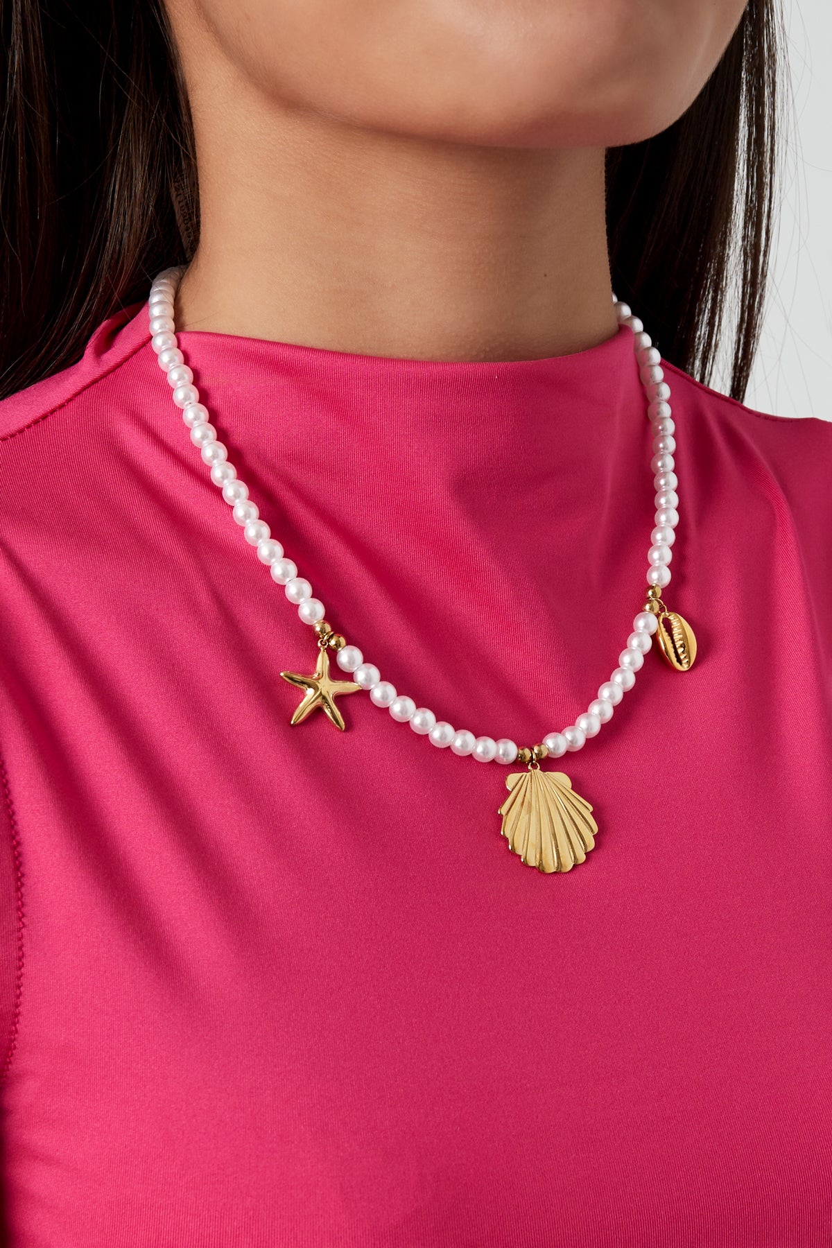 Model wearing pearl charm necklace with gold sea-themed charms paired with vibrant pink top