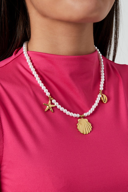 Model wearing pearl charm necklace with gold sea-themed charms paired with vibrant pink top