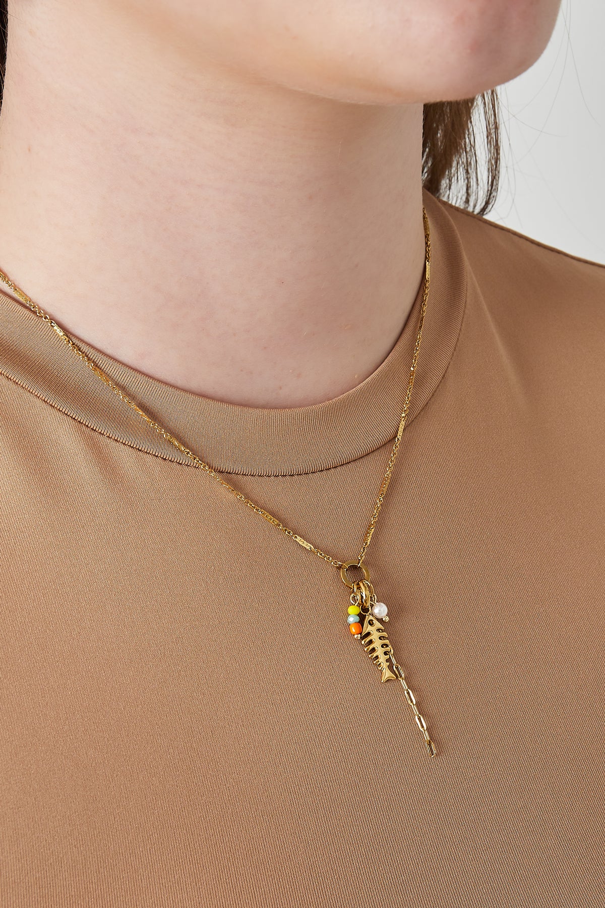 Close-up of a woman wearing the gold fish necklace over a beige top, showing playful colourful beads and pendant detail