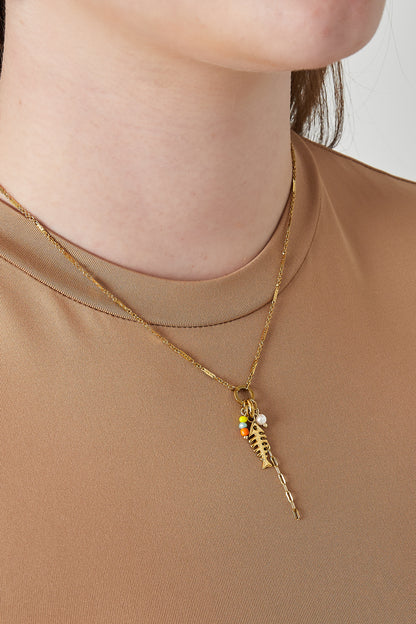 Close-up of a woman wearing the gold fish necklace over a beige top, showing playful colourful beads and pendant detail