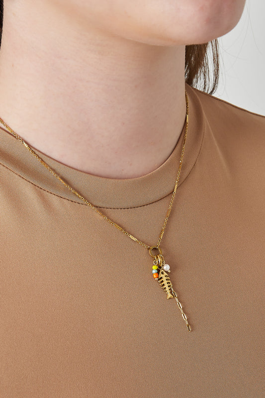 Close-up of a woman wearing the gold fish necklace over a beige top, showing playful colourful beads and pendant detail