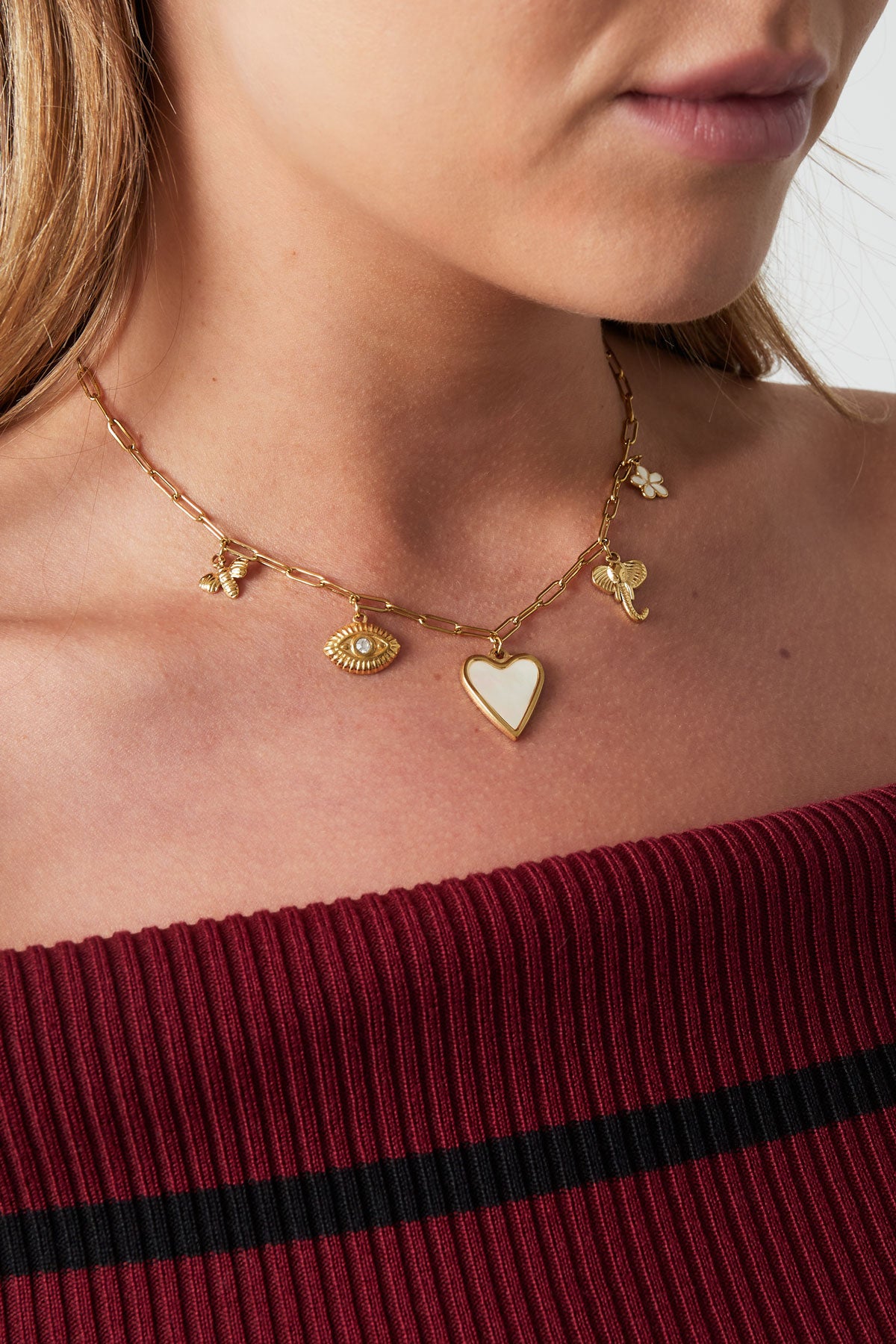 Close-up of a woman wearing the gold tone charm pendant necklace styled with a ribbed off-shoulder burgundy top