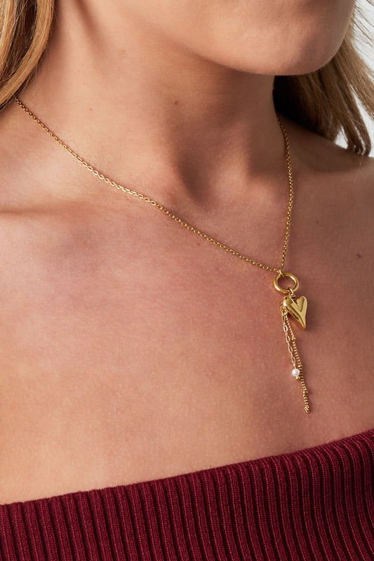 Close-up of woman wearing gold heart charm pendant necklace with dangling chain detail