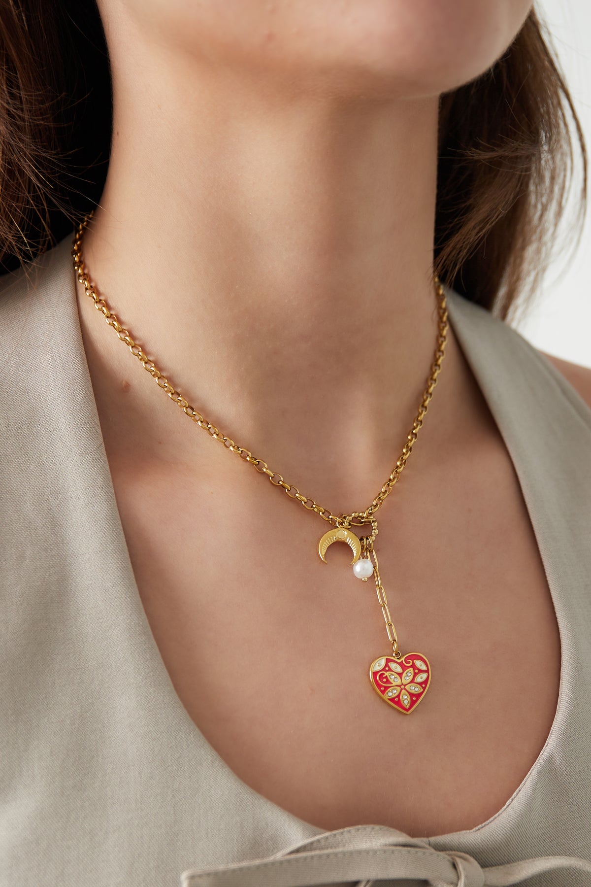 Model wearing the gold-tone charm necklace with red heart, crescent moon, and pearl on beige top
